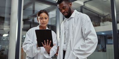 Two scientists standing in lab looking at tablet together