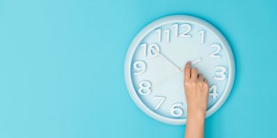 Human hand adjusting a clock on a blue wall